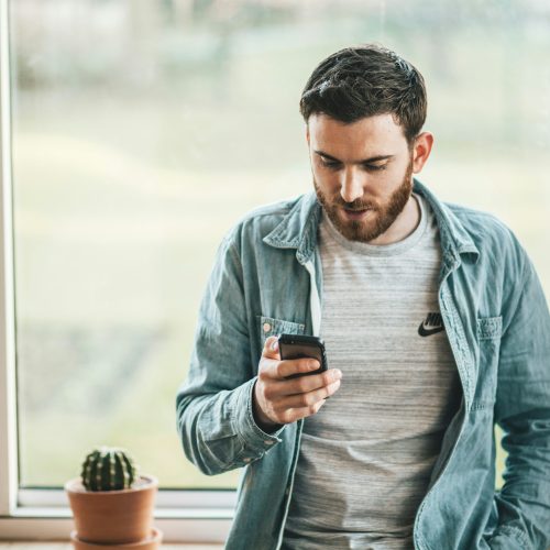 Man with a beard on the phone in front of a window Man with a beard on the phone in front of a window