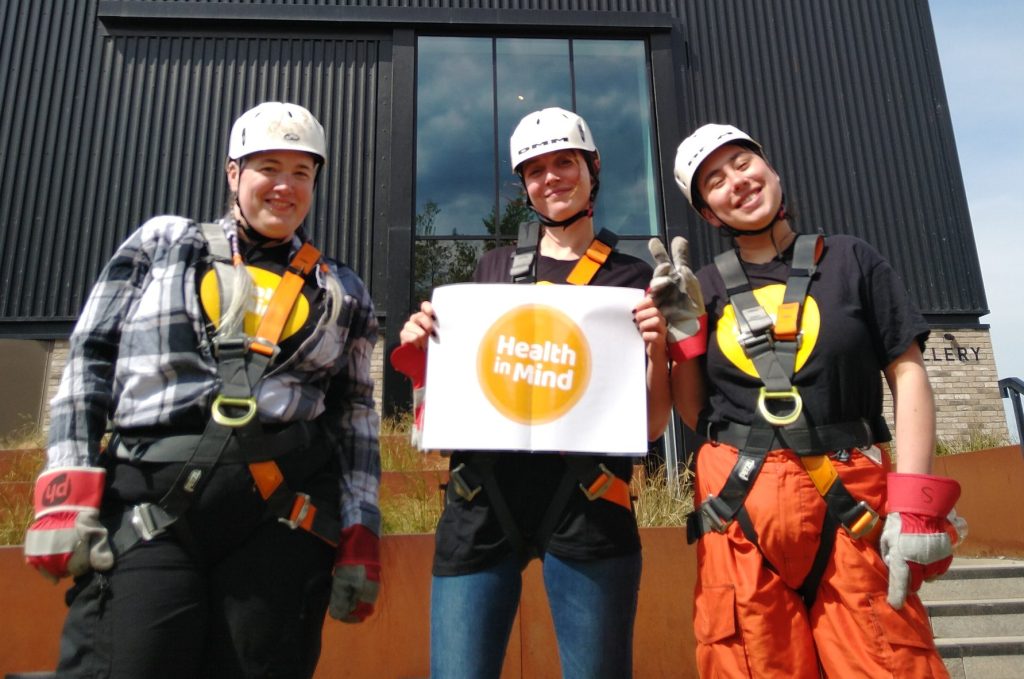 Three people in Health in Mind t-shirts, helmets and abseiling harnesses. Three people in Health in Mind t-shirts, helmets and abseiling harnesses.